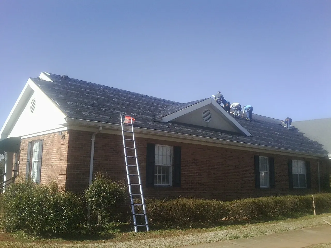 Crew tearing shingles off a brick ranch roof with a ladder set — Metal Roof Repair work by our crew in Oaks