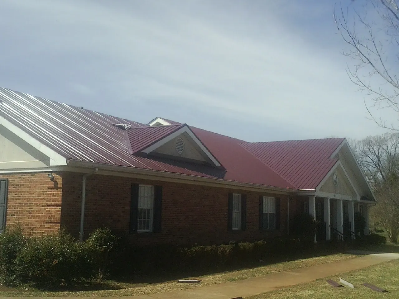 Red metal roof with gabled entries on a long brick building, from a Hail Damage Roof Repair job in Oaks