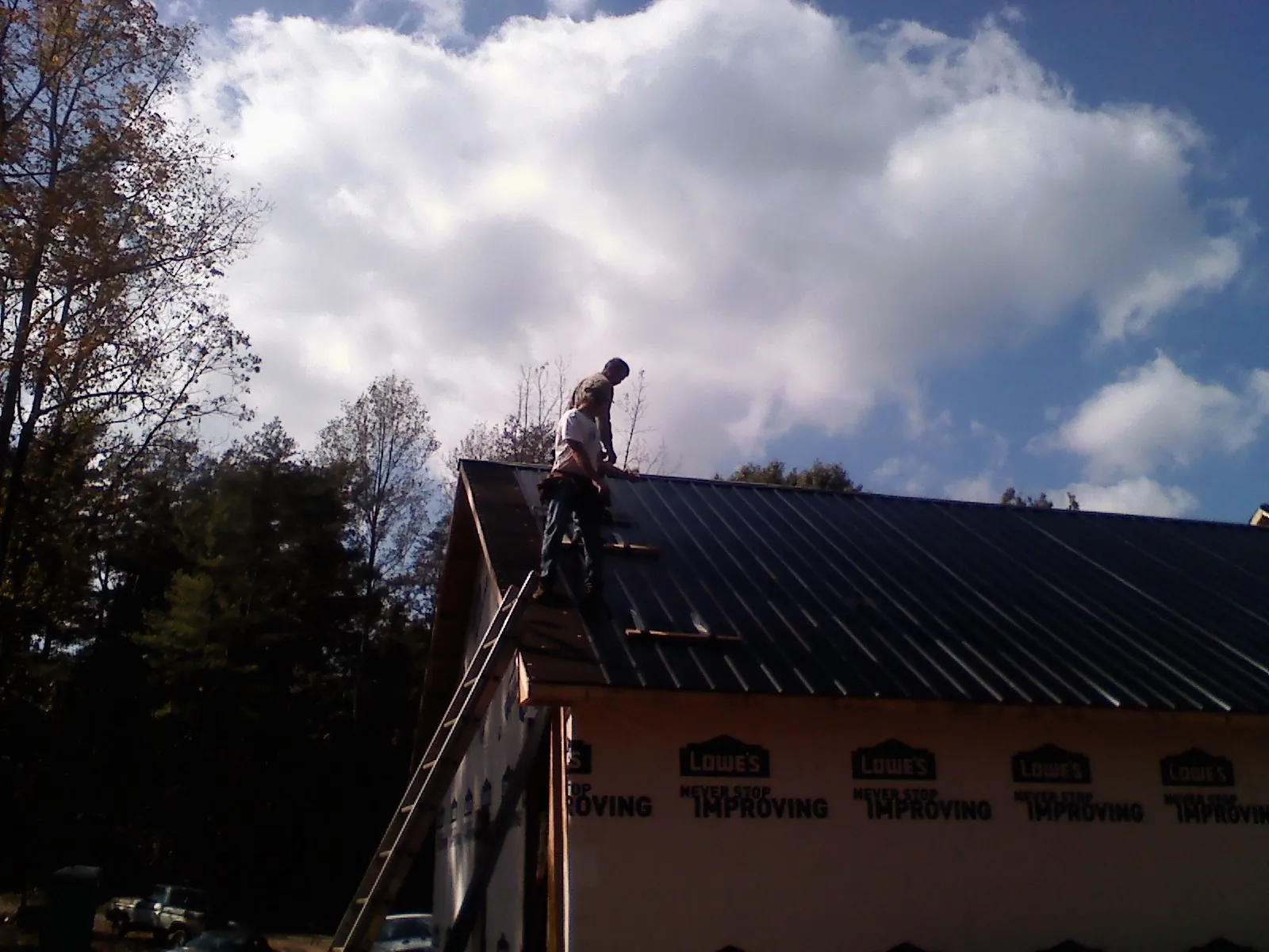 Roofer fastening dark metal panels high against a cloudy sky, from a Roof Inspection job in Oaks