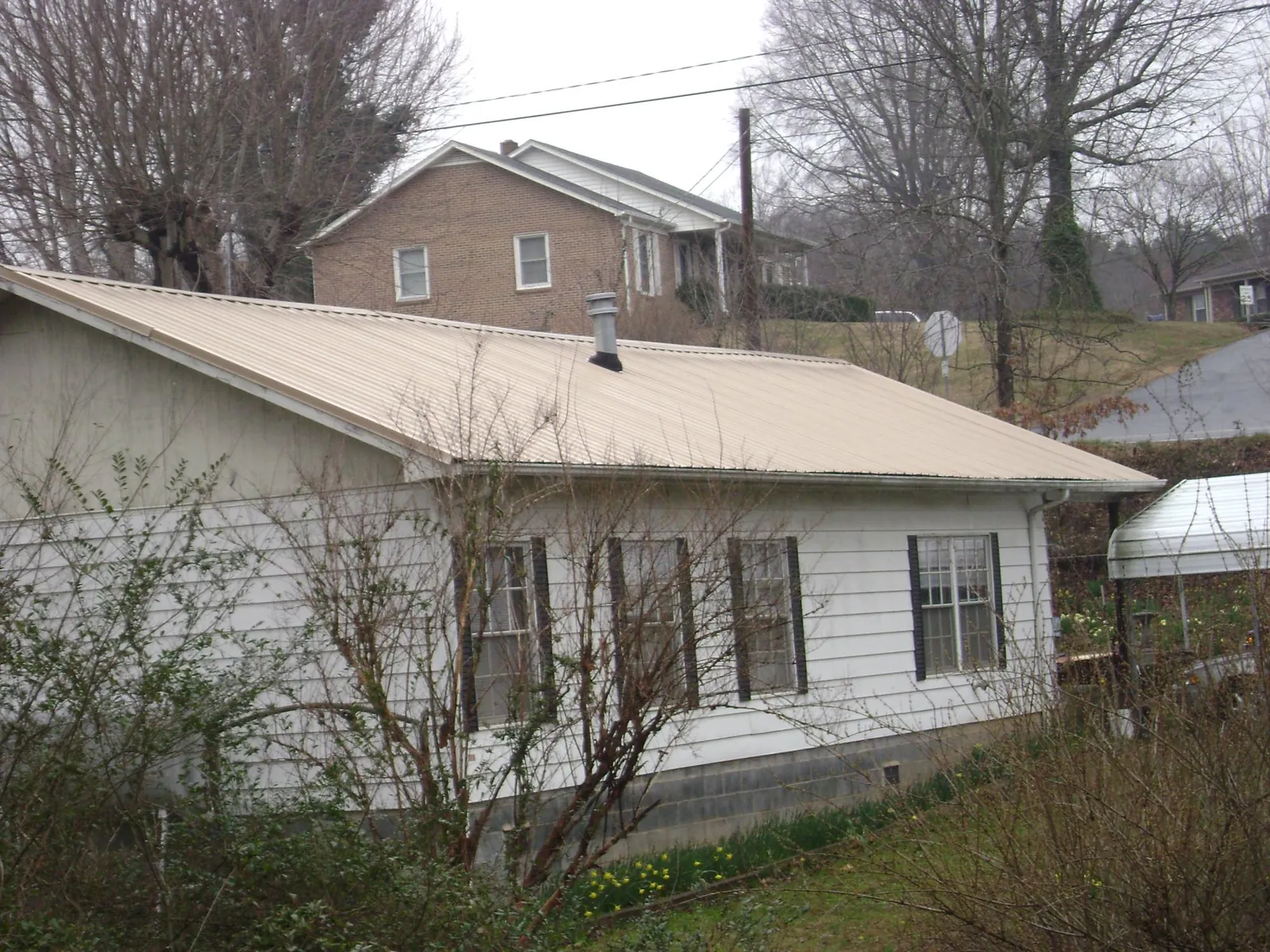 Tan metal roof on a white sided house set into a hillside — Commercial Roofing by Roofing Brothers in Oaks