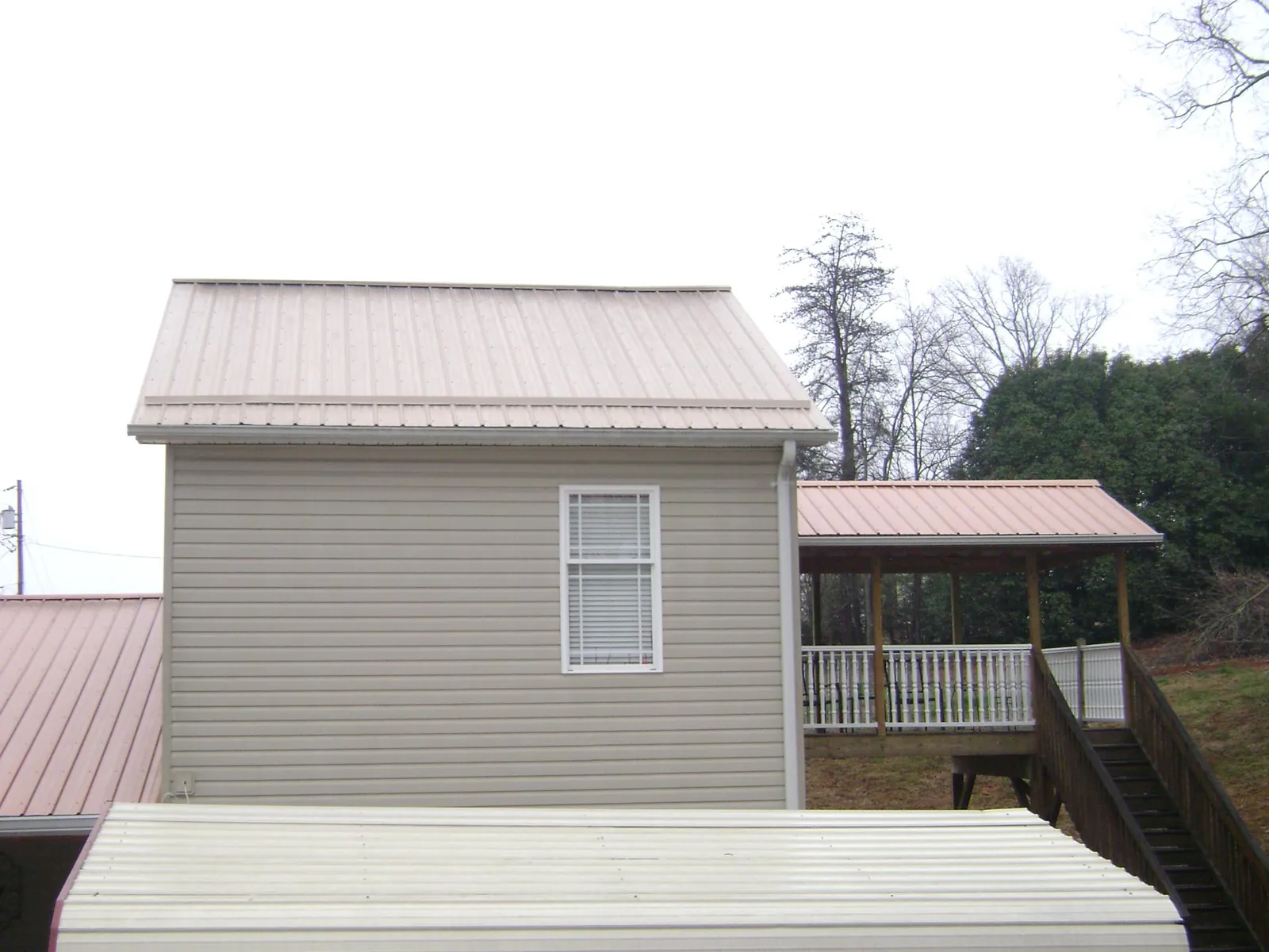 Tan metal roofs on a two story addition and attached porch, from a Roof Replacement job in Oaks